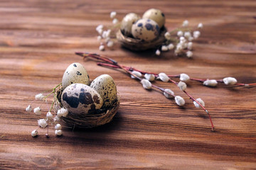 quail eggs in nests and willow branches on wooden surface