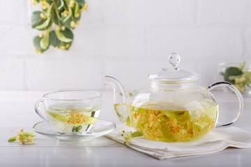 Linden tea in a transparent tea pot.  Glass tea pot with herbal lime tree tea on white background. Medicinal plant, flowers used for herbal teas and tinctures.