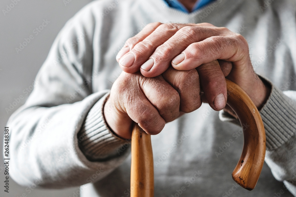 Hands of an elderly man resting on a walking cane - obrazy, fototapety, plakaty 