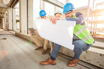 Wall Mural - Team of successful young architects and business partners having a meeting on a construction site. Looking at building floor plans