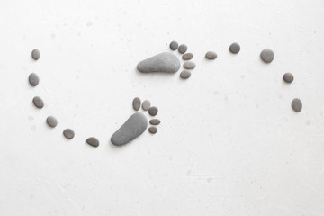 Footprints made of stones. Happy feet. Stone arranged like footprints on the beach. Spa background with grey stones. Copy space for your text. Aromatherapy for beauty, relaxation, nature massage