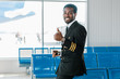 smiling african american pilot showing thumb up in departure lounge