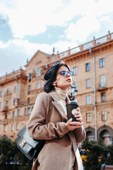 Beautiful elegant woman in sunglasses and coat with coffee in city