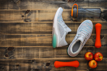 Wall Mural - Fitness, healthy and active lifestyles love concept, dumbbells, sport shoes, bottle of waters and apples on wood background. Top view with copy space.