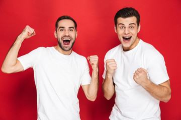 Wall Mural - Image of two joyous men friends 30s in white t-shirts rejoicing and clenching fists at camera