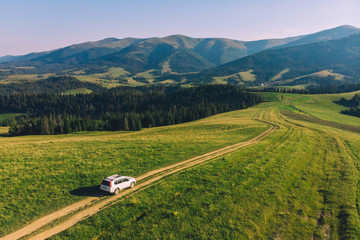 Wall Mural - white suv car in mountains at path trail on sunset