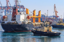 Tugboat Assisting Cargo Ship Maneuvered Into The Port Of Odessa, Ukraine. Handling Of Goods And The Work Of A Commercial Port.