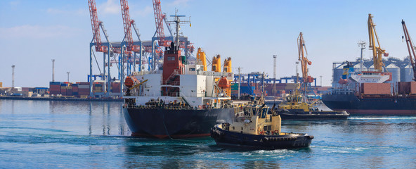 Wall Mural - Tugboat assisting Cargo Ship maneuvered into the Port of Odessa, Ukraine. Handling of goods and the work of a commercial port.