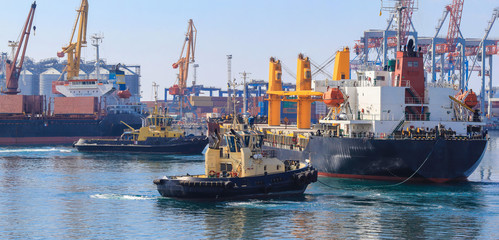 Wall Mural - Tugboat assisting Cargo Ship maneuvered into the Port of Odessa, Ukraine. Handling of goods and the work of a commercial port.