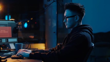 cybercrime, hacking and technology concept - asian male hacker writing code or using computer virus program for cyber attack and drinking coffee in dark room at night