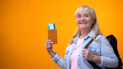 Joyful retiree woman showing passport and tickets, preparing for travel tour