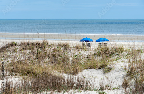 Cuadros en Lienzo A beachfront view of two blue beach umbrellas and chairs