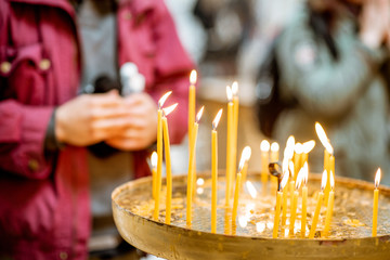 Burning candles with praying man on the background in the church