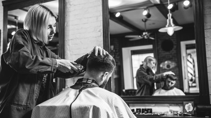 Wall Mural - Young woman making haircut for bearded man at barbershop. Female barber at salon. Gender equality. Woman in the male profession. Black and white or colorless photo. Hairstyle, salon, hairdresser