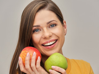 woman smiling with healthy teeth holding two apples.