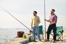 Leisure And People Concept - Happy Friends With Fishing Rods And Beer On Pier At Sea