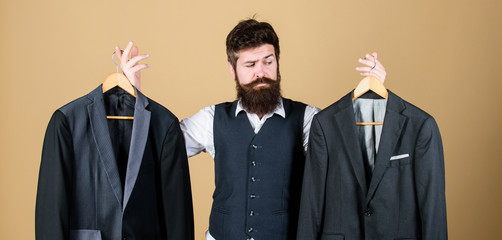 Doubting about his choice. Bearded man holding suit jackets in store, choice concept. Hipster making shopping choice in shop. Businessman choosing which formal suit to wear. Choice of clothes