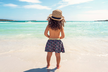 little girl with her back on a white sand beach