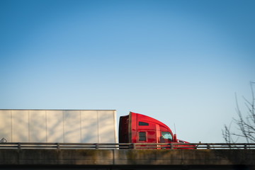 Wall Mural - Semi truck on highway at sunset red tractor with blue sky