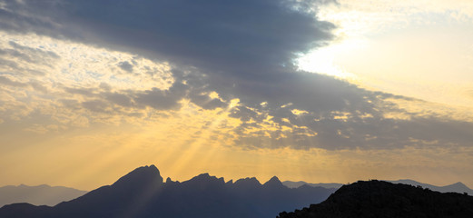 Wolken mit Sonne hinter Gebirge