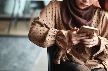 Wall Mural - Muslim female using mobile phone and sitting on office room.