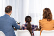 © LIGHTFIELD STUDIOS - back view of parents sitting near daughter on chairs