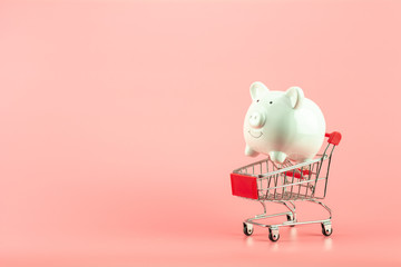 white piggy bank in small shopping cart on pink background. - save and management concept.