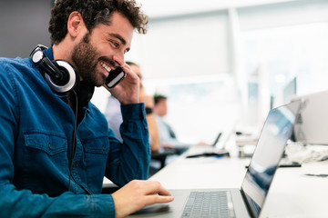 Handsome man using phone and laptop in a modern office.