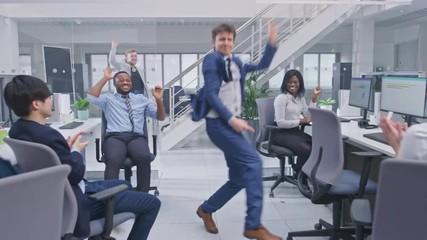 Poster - Young Happy Business Manager Wearing a Suit and Tie Dancing and Giving High Fives in the Office. Celebrating Success. Diverse and Motivated Business People Work on Computers in Modern Open Office.