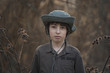 © Sergey Kohl - A boy in a hat and coveralls is standing in dry bushes of burdock.