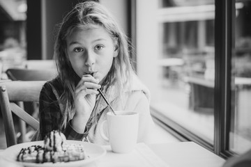 Happy nice little girl at cafe.The child sits at a table in a cafe and is happy.A happy childhood, concept of coziness and children, cold season, holidays 