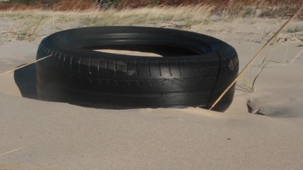 Wall Mural - This car tire is thrown on coastal dunes by sea surf. Grains of sand bombard wheel constantly and polished to shine. The concept of strength and reliability of automobile tires, but sea is polluted