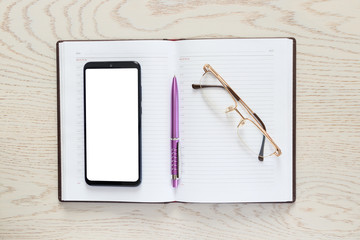 Smartphone with isolated empty white screens for design on an organizer diary with glasses and pen on the background of a wooden table