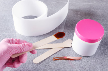 Cosmetologist in pink protective gloves holding stick with wax for depilation.Concept of preparation for waxing treatments