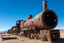  A Head On Shot A Rusting Steam Trains And Carriages  That Are Slowly Rot Away At The Train Graveyard Just Outside Of Uyuni, Bolivia, Against A Bright Blue Sky.