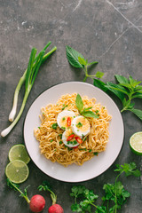 Dry instant noodles put egg with fresh herbs, garnish of cilantro and Asian basil, lemon, lime on dark stone background