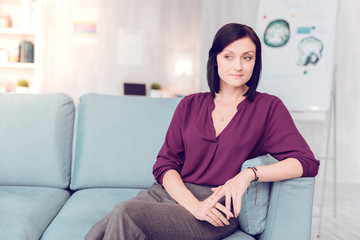 Beautiful dark-haired elegant woman sitting on a living room couch.