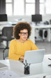 © nenadaksic - Serious mixed race businesswoman dressed casual sitting in modern office and using laptop.