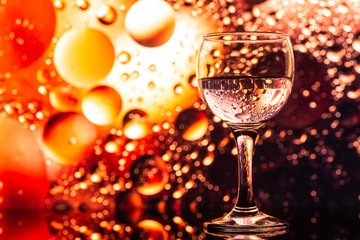 transparent glass with water and oily drops on purple background 