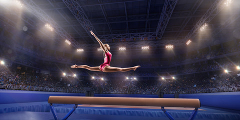 Female athlete doing a complicated exciting trick on gymnastics balance beam in a professional gym. Girl perform stunt in bright sports clothes