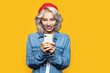Portrait of charming blonde girl texting with someone on smartphone. Fashionably dressed lady in jacket. Communication and lifestyle concept. Isolated on yellow background