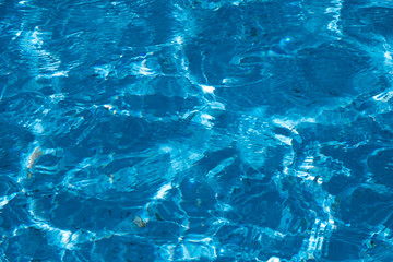 blue and bright ripple water surface in swimming pool with sun reflection.