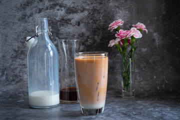 Hand of woman holding grass of green tea and pouring into a glass of milk with black concrete in background.