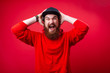 © Vulp - Handsome frustrated guy with beard screaming and putting hand on head, standing over red isolated  background