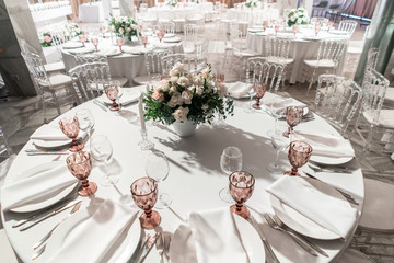 Interior of restaurant for wedding dinner, ready for guests. Round Banquet table served. Decorated with floral arrangement. Dishes, wine glasses and napkins. Catering concept.