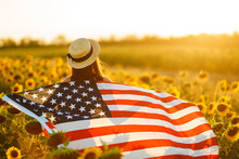 Beautiful Girl In Hat With The American Flag In A Sunflower Field. 4th Of July. Fourth Of July. Freedom. Sunset Light The Girl Smiles. Beautiful Sunset. Independence Day. Patriotic Holiday. 