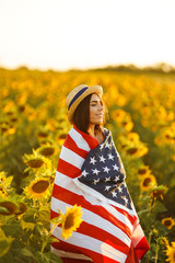 Beautiful girl in hat with the American flag in a sunflower field. 4th of July. Fourth of July. Freedom. Sunset light The girl smiles. Beautiful sunset. Independence Day. Patriotic holiday. 