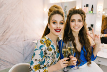 Portrait Two Attractive Joyful Models With Stylish Makeups, Luxury Coiffures Having Fun, Drinking Champagne In Haidresser Salon. Friends Together, Expressing True Positive Emotions, Joy, Beauty
