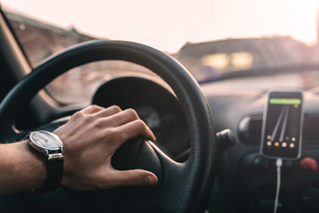 Wall Mural - driver with a wristwatch rides through the city using a navigator on a smartphone on a sunny day.