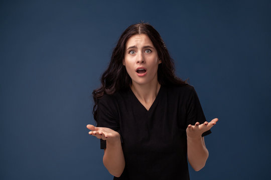 Portrait of a long-haired brunette woman in black t-shirt posing on a gray background and showing different emotions.